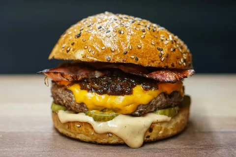 Hambúrguer com queijo derretido, bacon e picles em pão com gergelim.